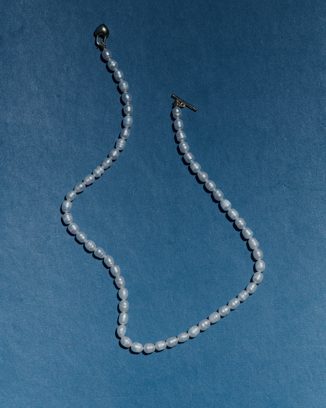 Freshwater pearl necklace with silver clasp on blue suede — jewellery still life photography Melbourne