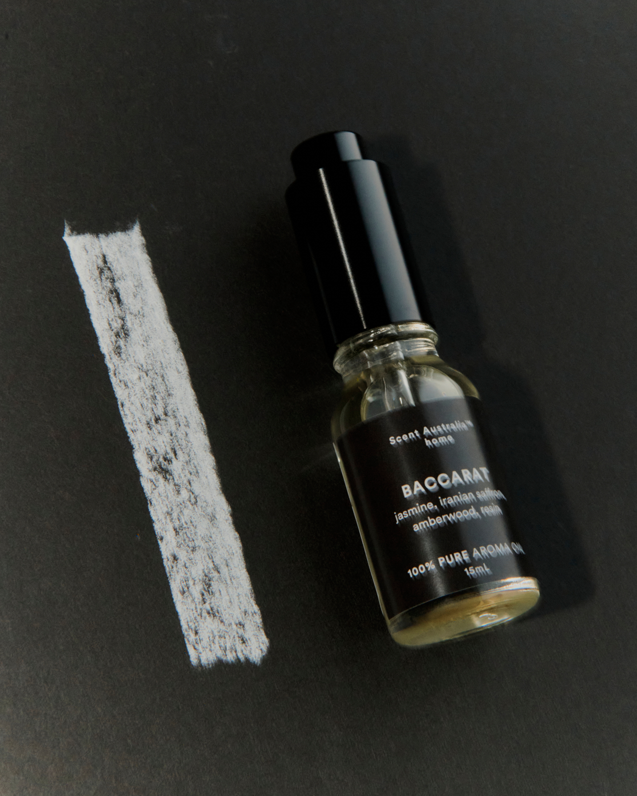 Reed diffuser glass tube and two black fibre sticks on pale surface — minimal still life