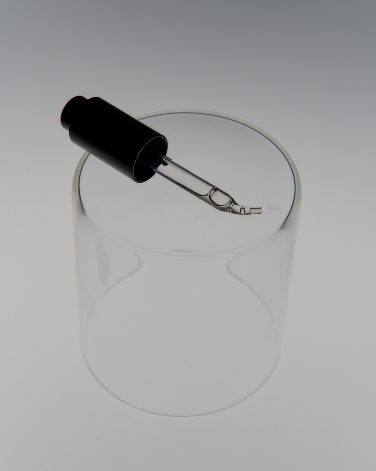 Glass pipette tip close-up with oil droplet forming — macro detail product photography