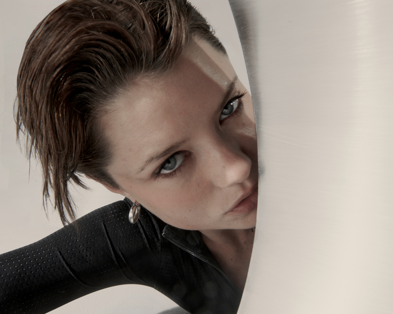 Close-up portrait — model peeking behind brushed metal sheet, fashion lookbook photography