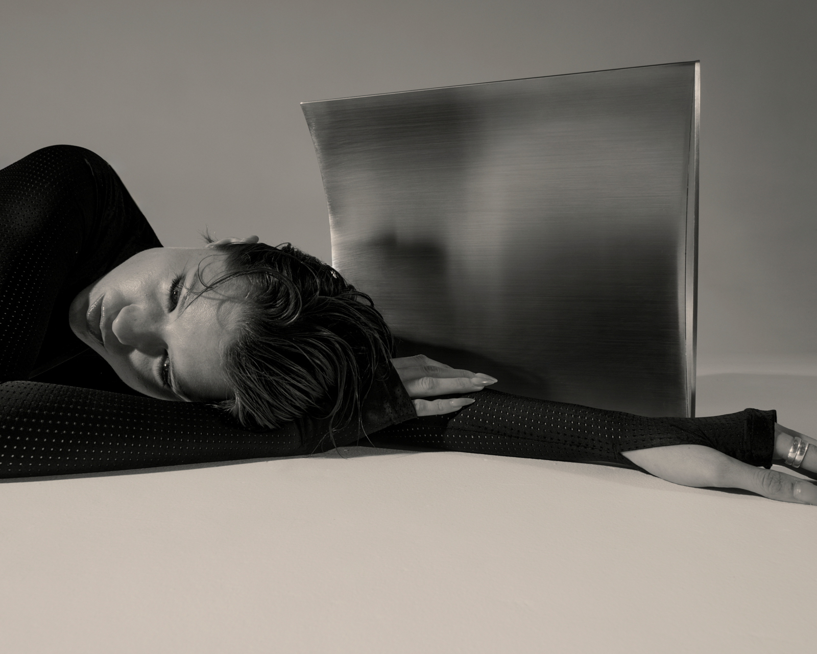 Model lying with brushed steel sheet — black and white fashion photography, custom set build
