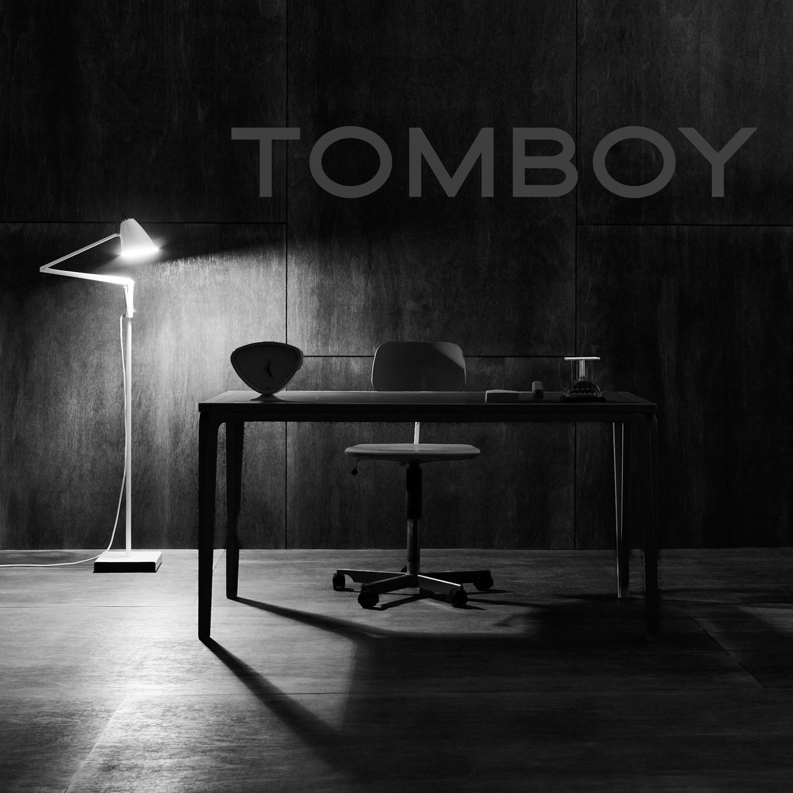 TOMBOY wordmark on the timber-panelled set above a desk, chair and floor lamp — black and white campaign image by Matthew Krueger